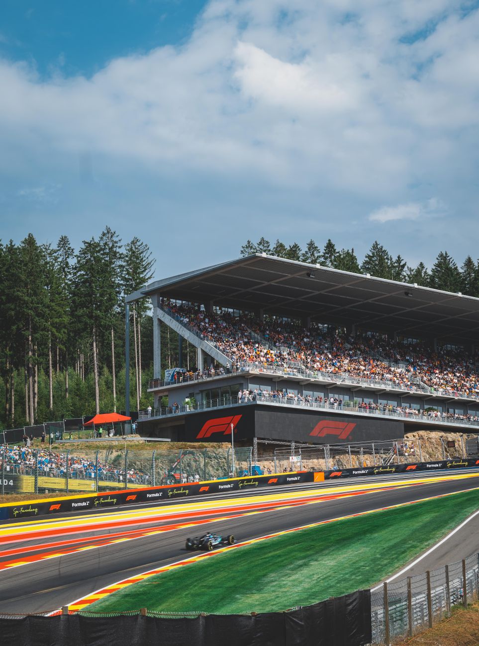 Een spannende Formule 1-race op het Circuit de Spa-Francorchamps in Stavelot, België, met een enthousiast publiek en een weelderig bos op de achtergrond.