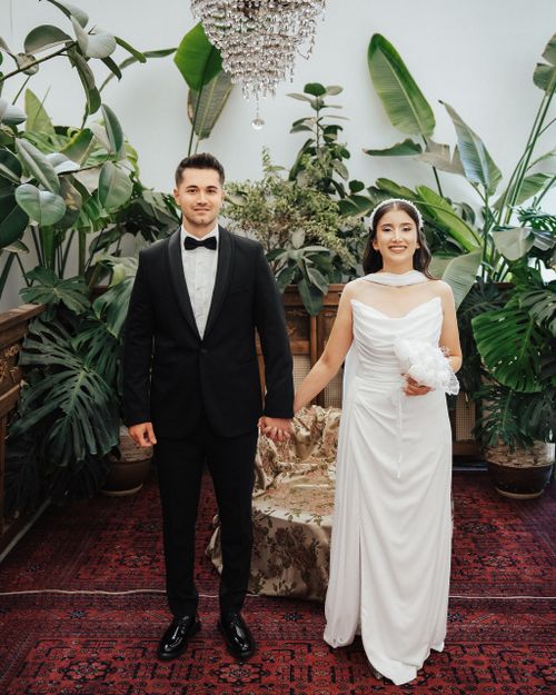 Free Bride and groom pose elegantly in a lush indoor garden decorated with tropical plants. Stock Photo