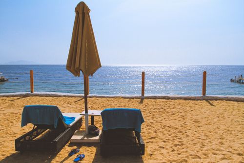 Free Tranquil sunny beach with two empty loungers and umbrella by the sea. Stock Photo