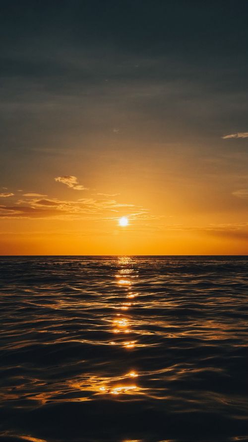 Free A mesmerizing view of the ocean at sunset with golden hues and calm waters creating a tranquil scene. Stock Photo