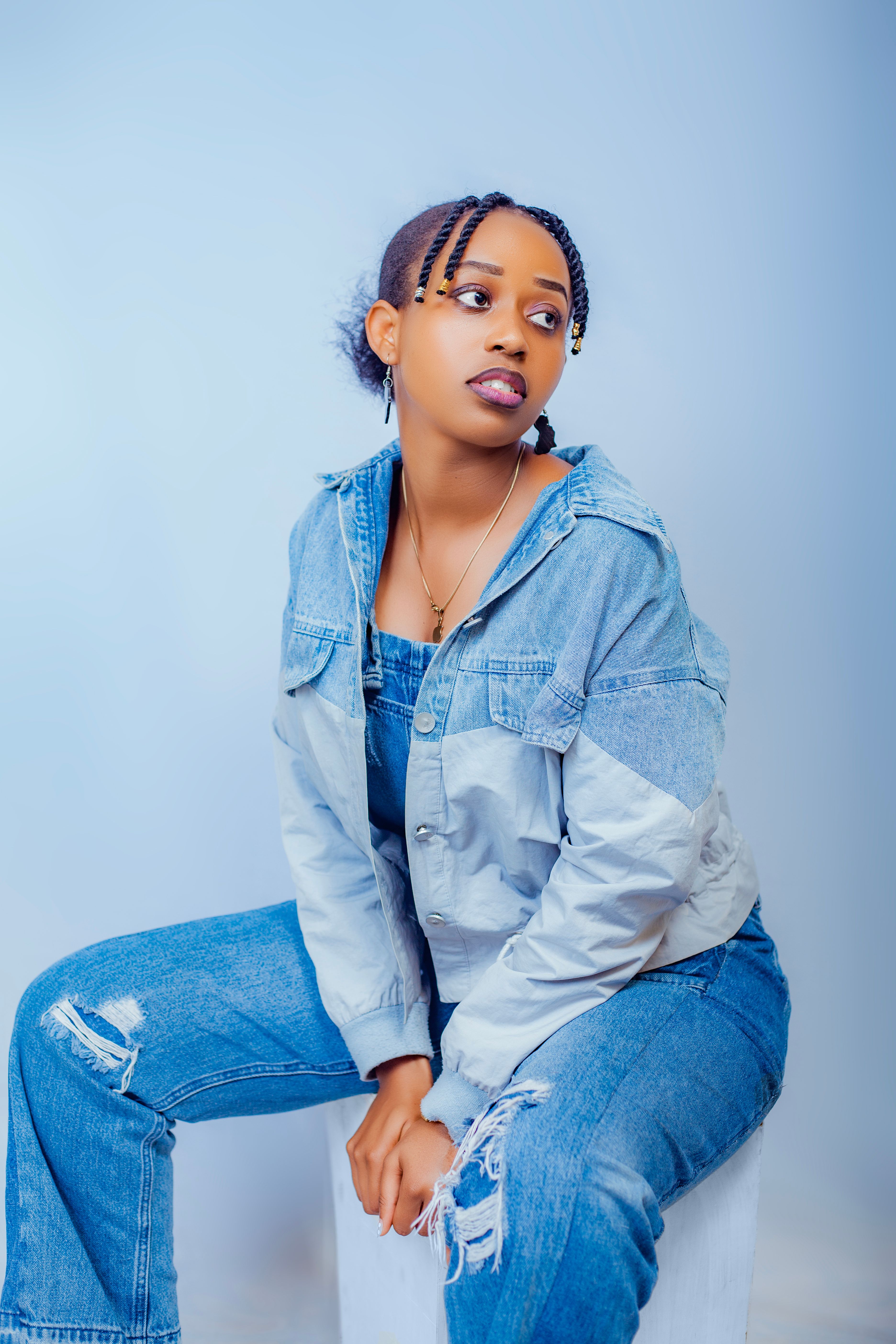 Stylish young woman in denim jacket and jeans posing against a light background.