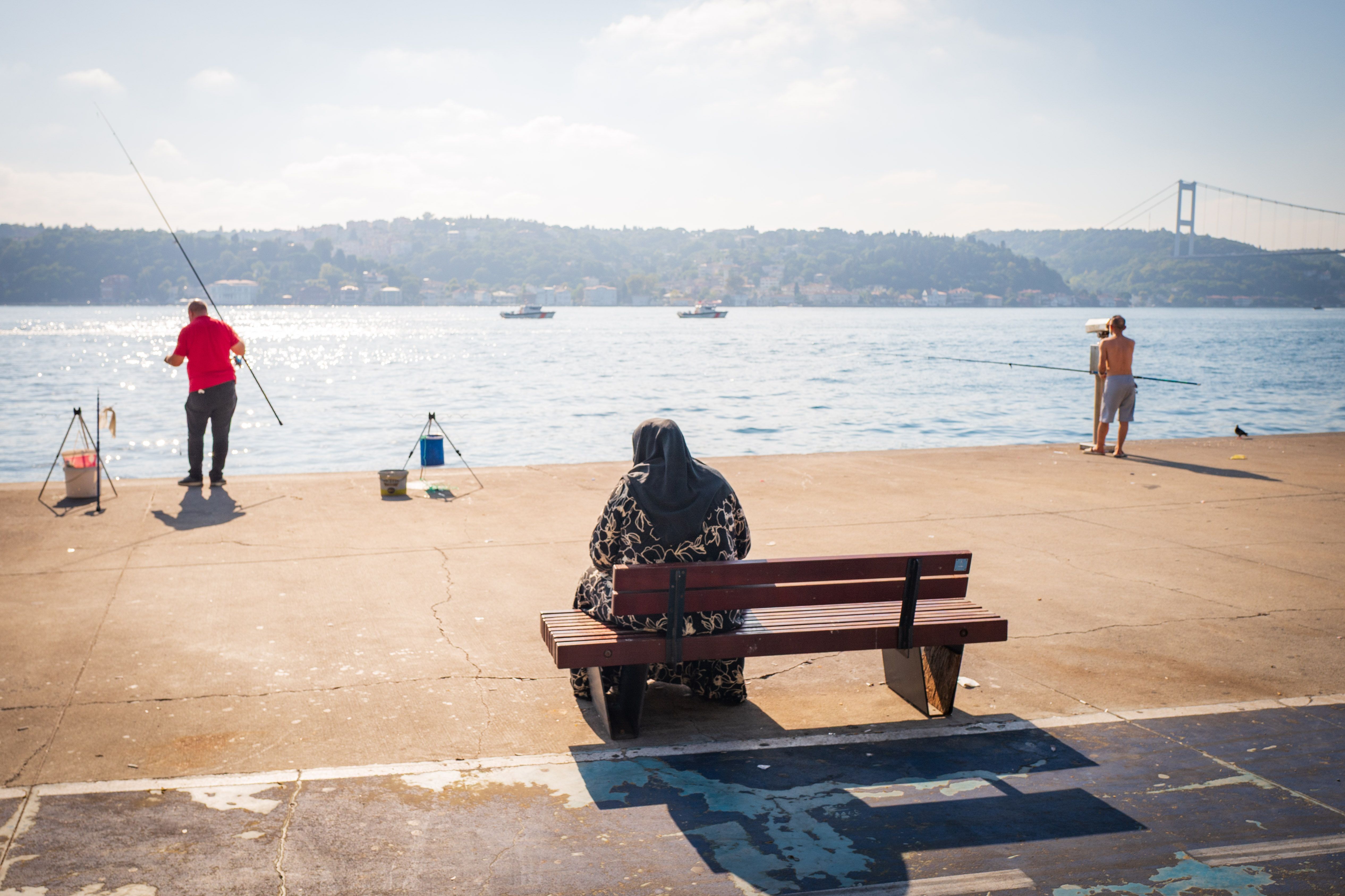 People fishing along the Bosphorus, overlooking city skyline and bridge in the distance.
