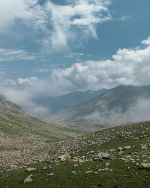 Free Serene mountain valley with misty clouds and vibrant green hills under a bright sky. Stock Photo