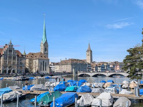 Beautiful daytime view of the Limmat River, Fraumünster Church, and covered boats in Zurich, Switzerland.