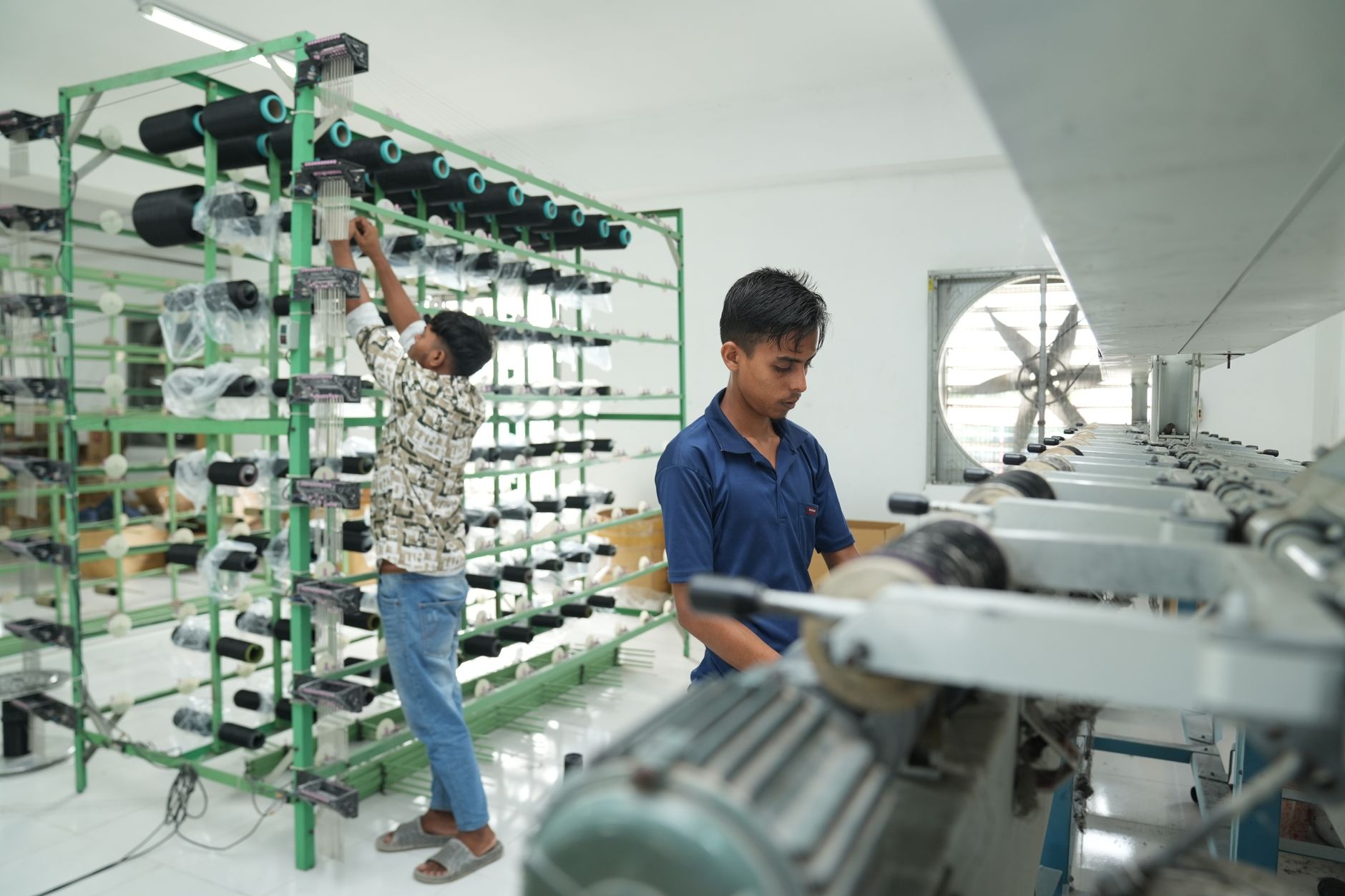 Two workers operate machinery in a textile factory, focusing on precision and efficiency.