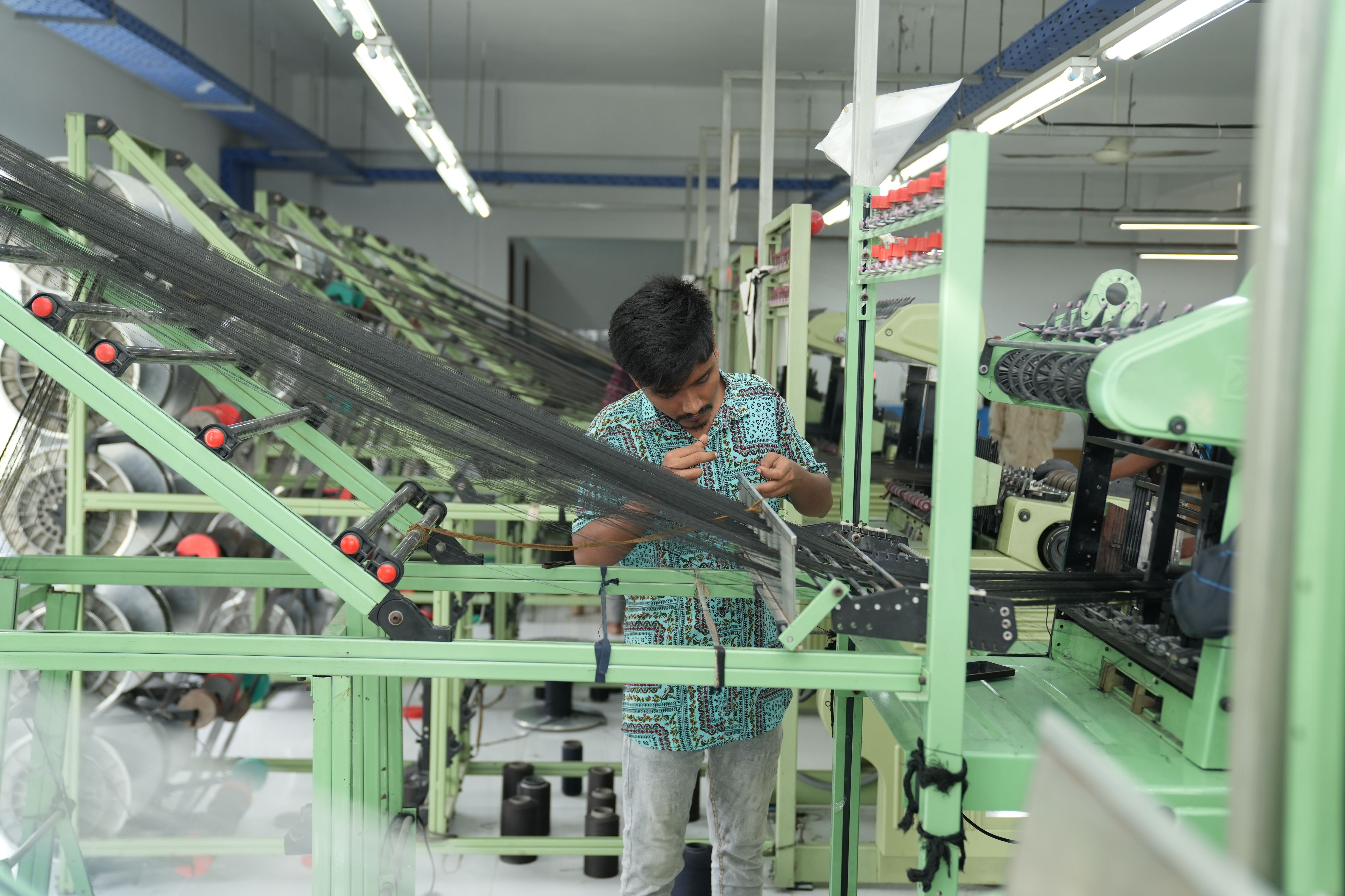 A worker in a textile factory adjusts threads on a modern weaving machine.