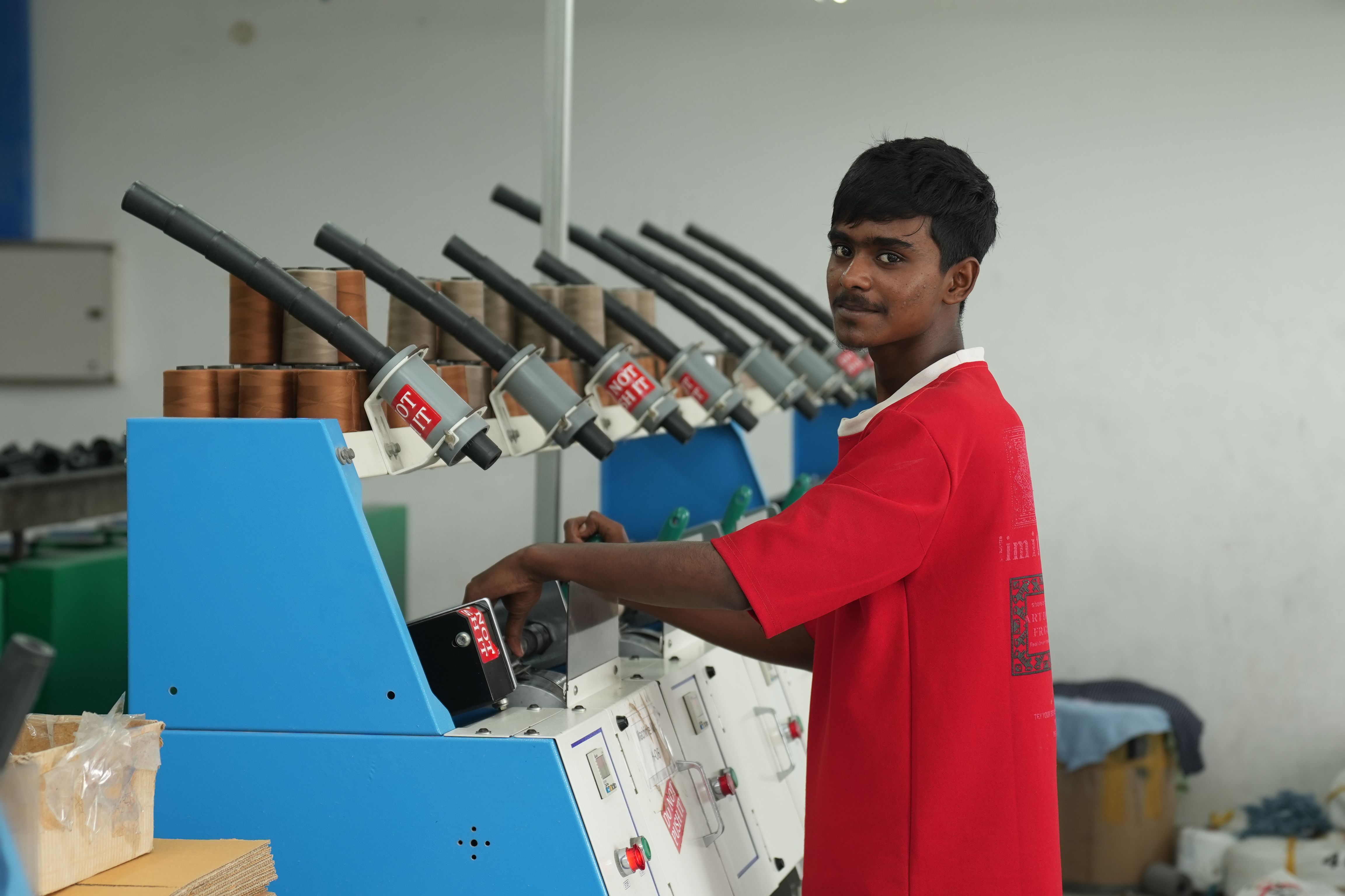 A young male factory worker in a red shirt operates a machine indoors, focusing on his task.