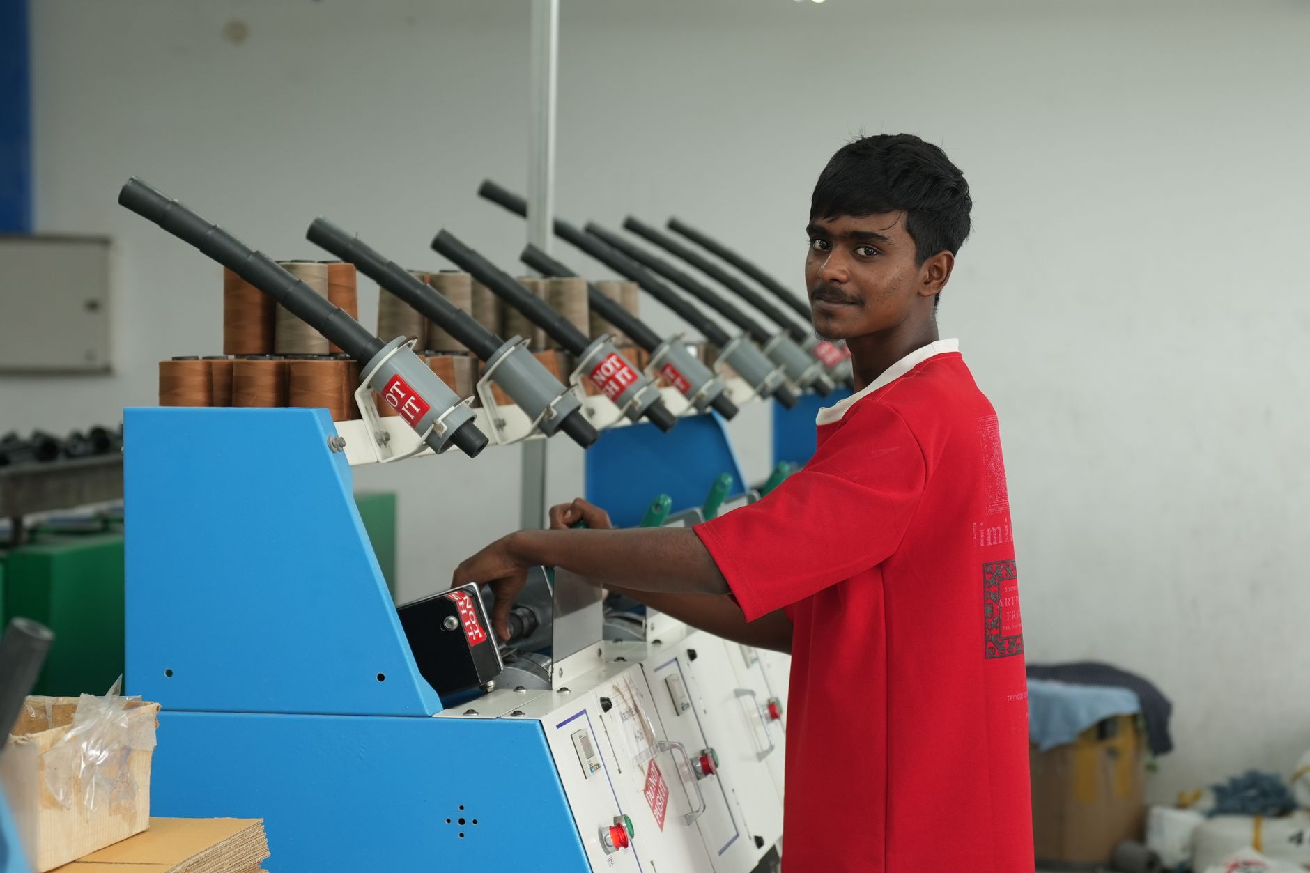 A young male factory worker in a red shirt operates a machine indoors, focusing on his task.