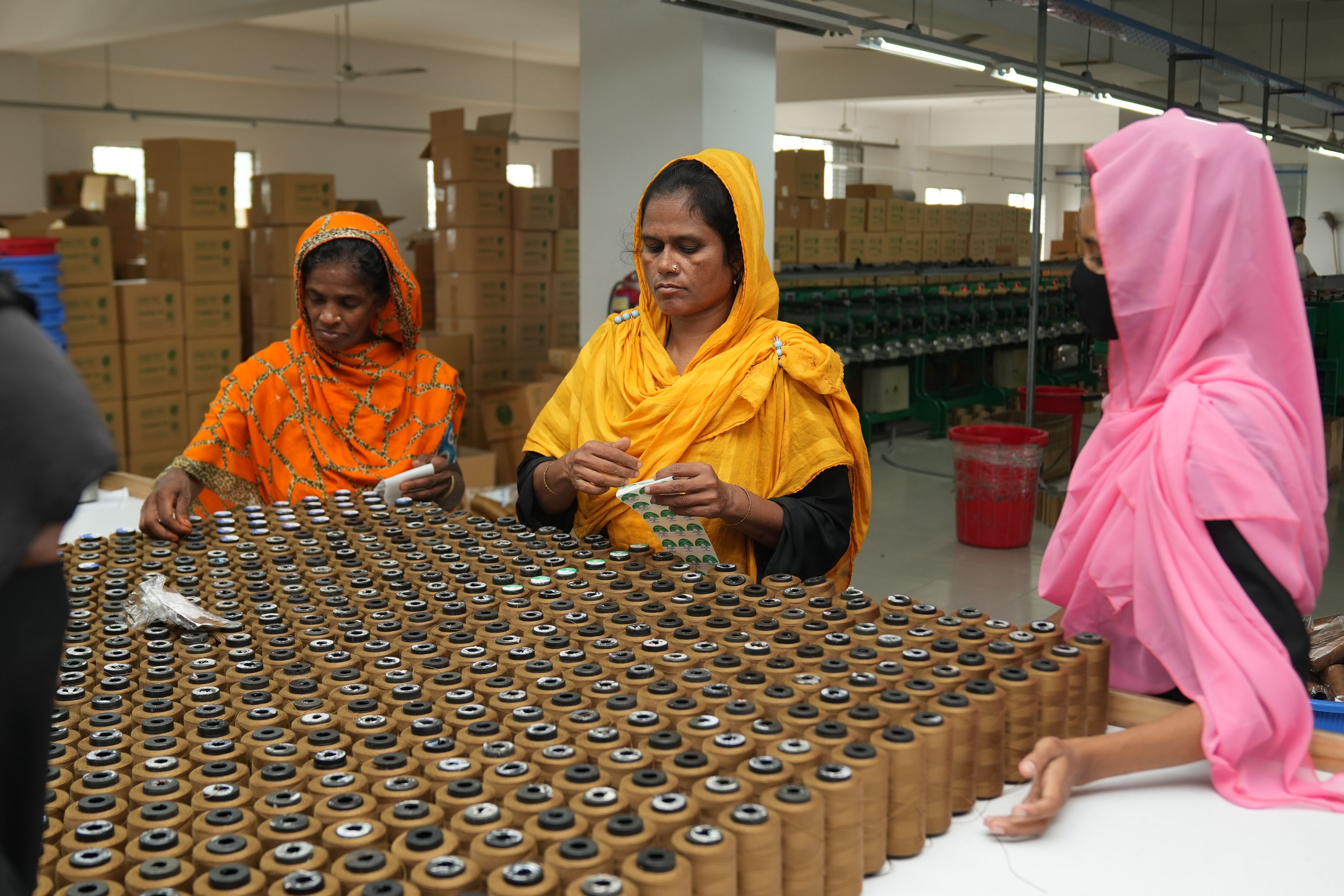 Four women sorting spools of thread in a bustling textile factory.