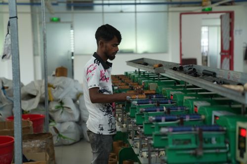 Free A focused worker operates textile machinery in a bustling factory setting, surrounded by material bags. Stock Photo