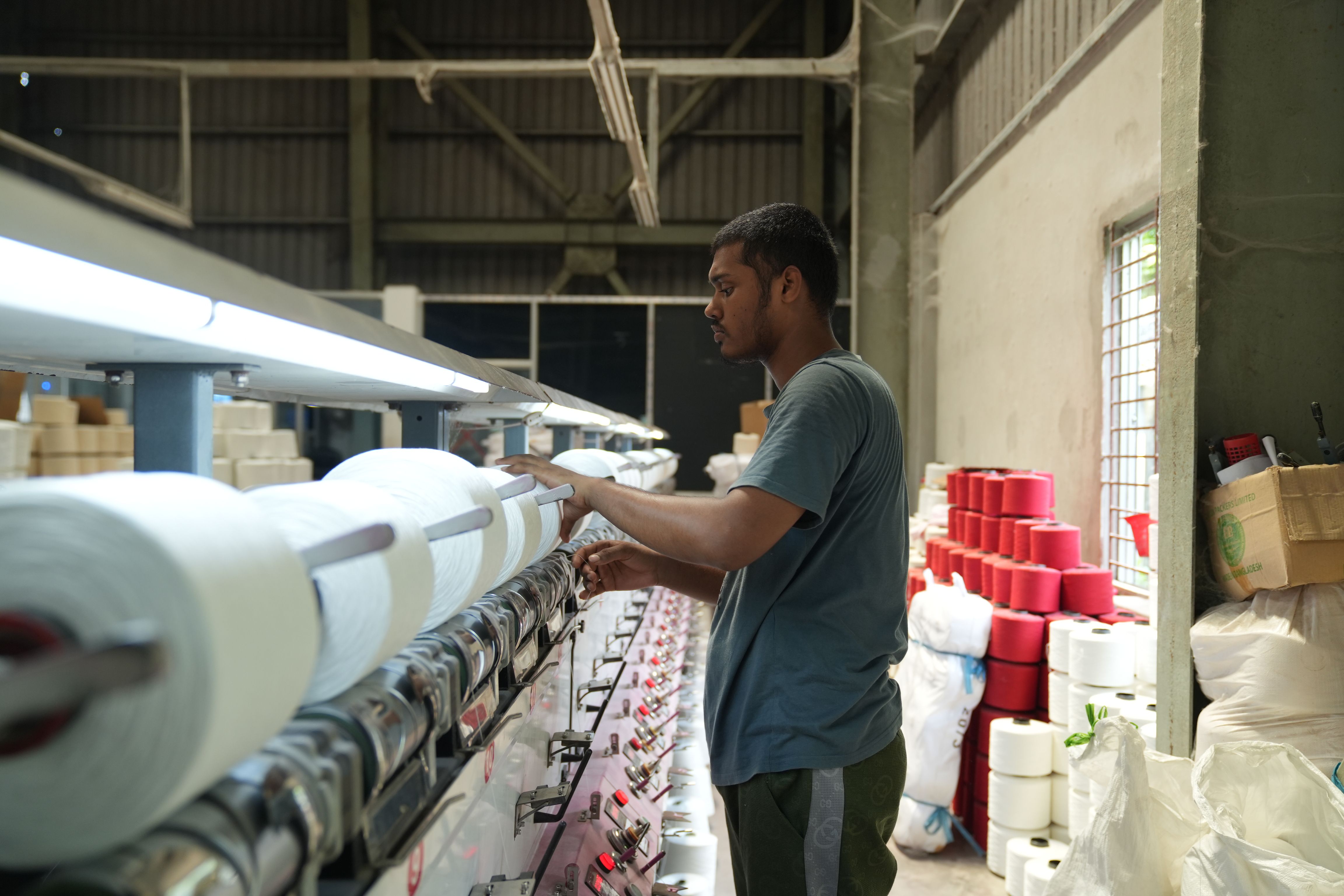 A textile worker adjusts spinning equipment in a well-lit factory, highlighting industrial efficiency.