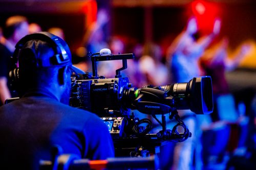 Free A cameraman using professional video equipment to film an event indoors. Stock Photo