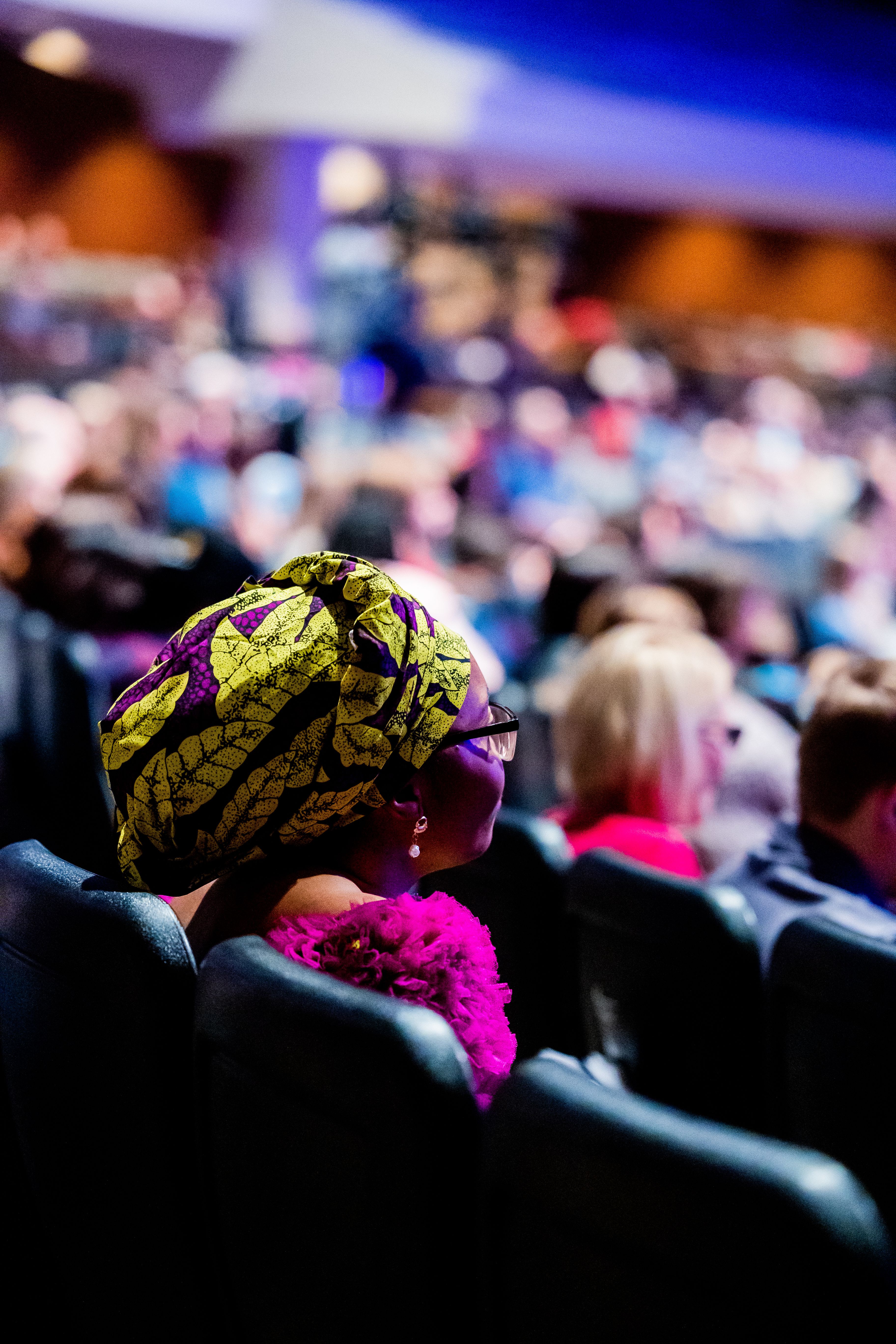 A vibrant conference audience with focus on a woman in a colorful headscarf, capturing cultural diversity.