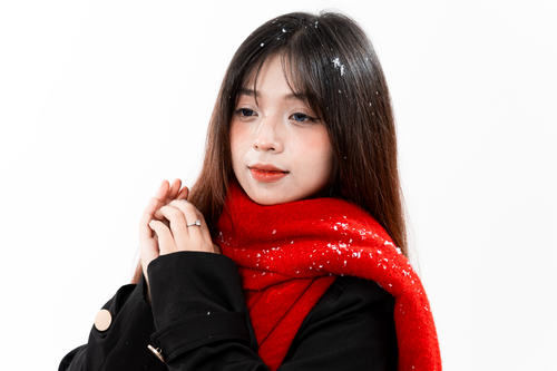 Free A young woman wearing a red scarf and black coat in a snowy winter setting. Stock Photo