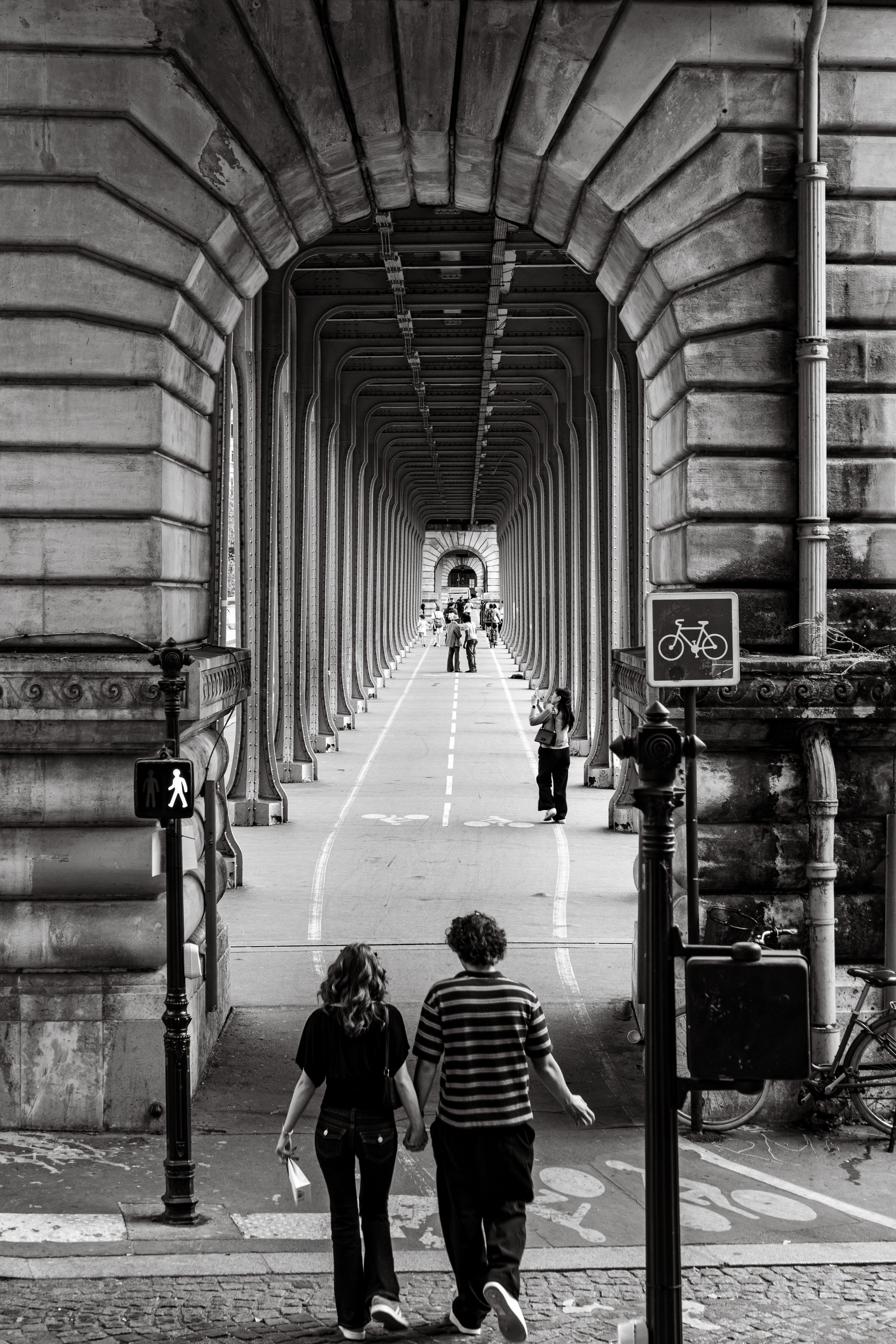 A couple holding hands walks through a historic bridge archway in Paris, France.