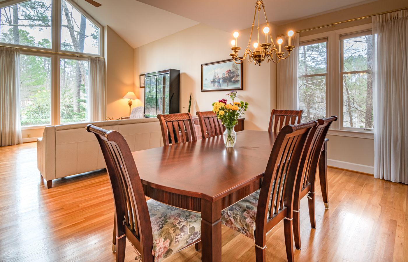 Bright indoor dining area showcasing dark wood furniture, large windows, and modern chandelier.