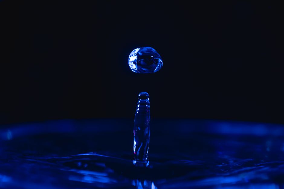 Capture of a water droplet splash in vivid blue light, showcasing high-speed photography.
