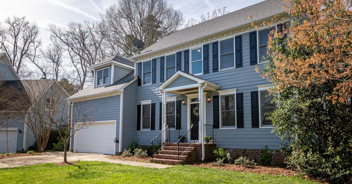 Spacious blue family home with garage, surrounded by trees and lush lawns in a suburban neighborhood.