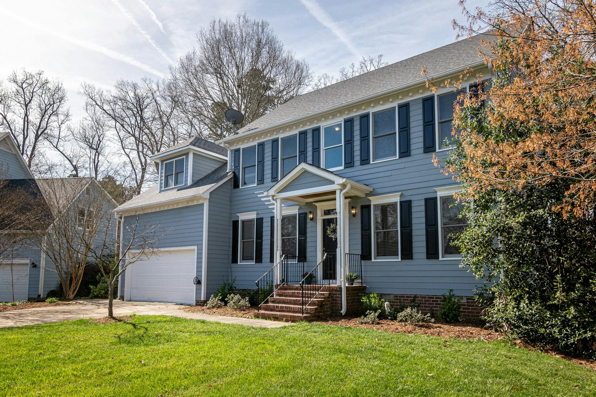 Spacious blue family home with garage, surrounded by trees and lush lawns in a suburban neighborhood.