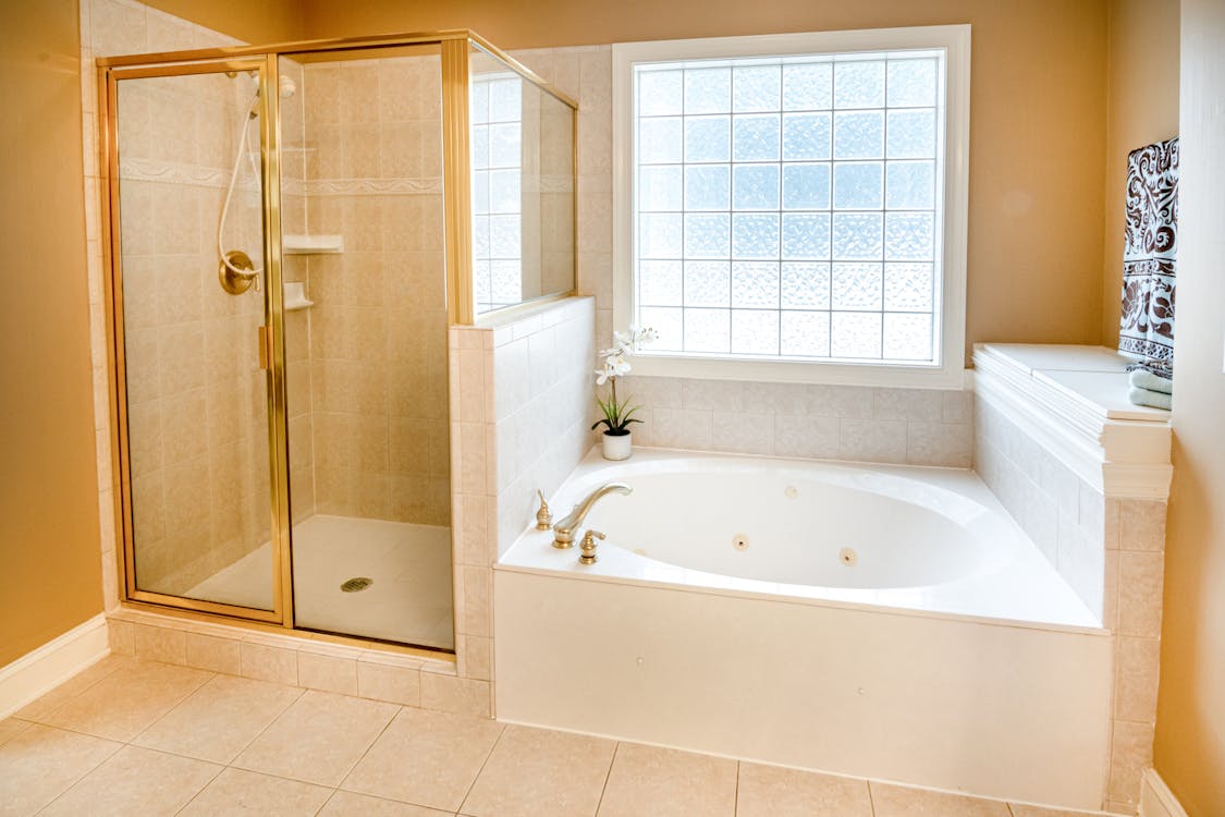 Ceramic Bathtub Near Window and Gold Framed Shower Stall