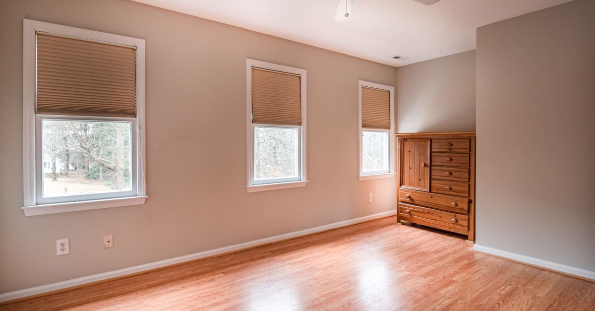 Spacious empty room with wooden flooring, natural light, and a wooden dresser. Ideal for interior planning.
