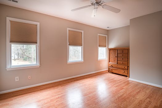 Spacious empty room with wooden flooring, natural light, and a wooden dresser. Ideal for interior planning.