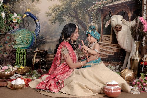Free A mother and child in traditional Indian attire, surrounded by peacock and cow statues in a decorative setting. Stock Photo