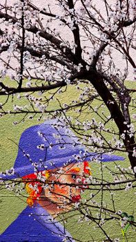 Colorful mural of a woman in a hat partially obscured by blooming cherry blossoms.