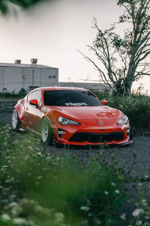 Free Bright red modified sports car parked outdoors, surrounded by greenery under a tranquil sky. Stock Photo