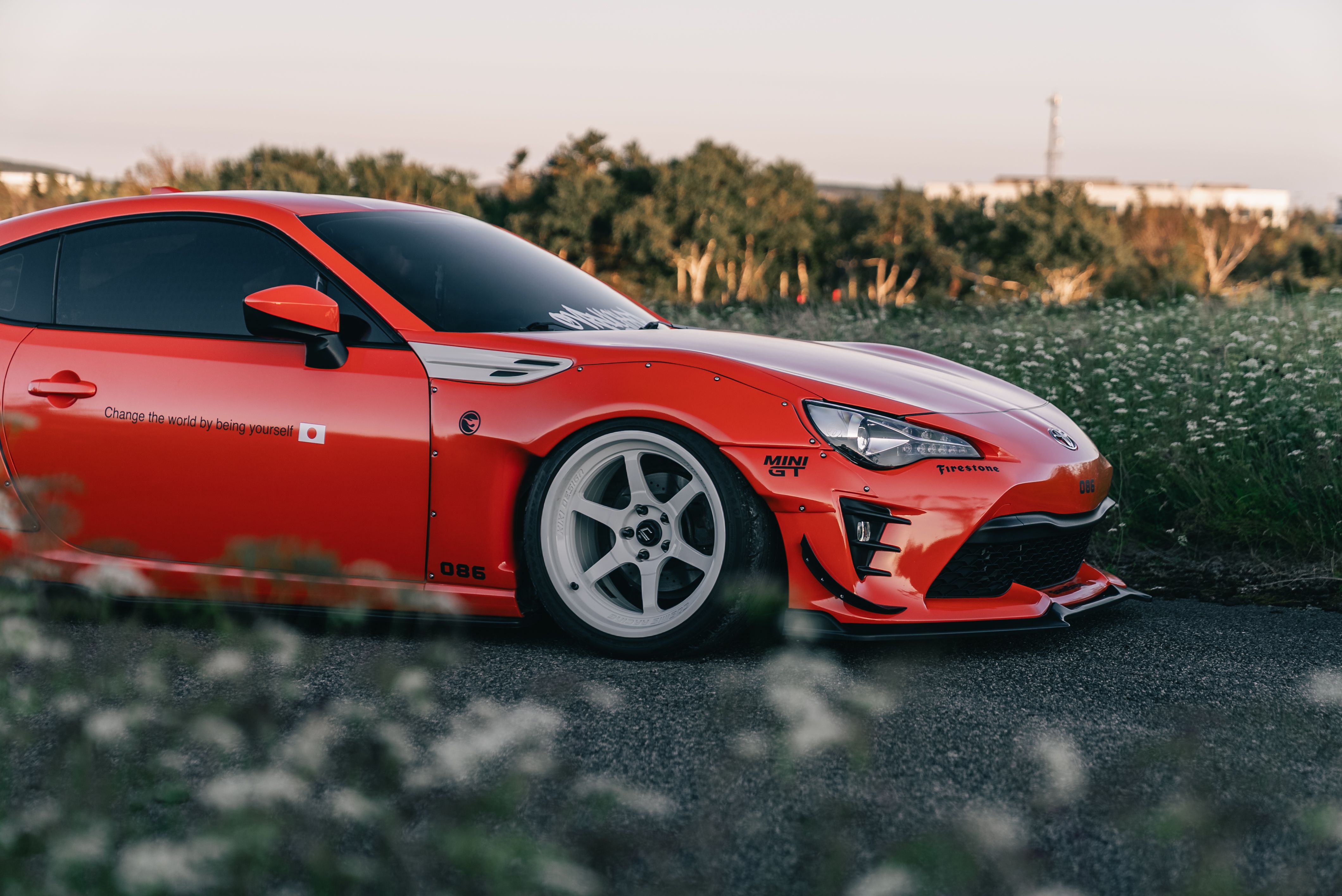 Side view of a sleek red sports car with custom decals parked on a scenic country road during sunset.