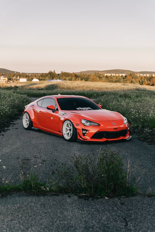 Free Stunning matte red sports car parked on a rural road during sunset surrounded by green fields. Stock Photo