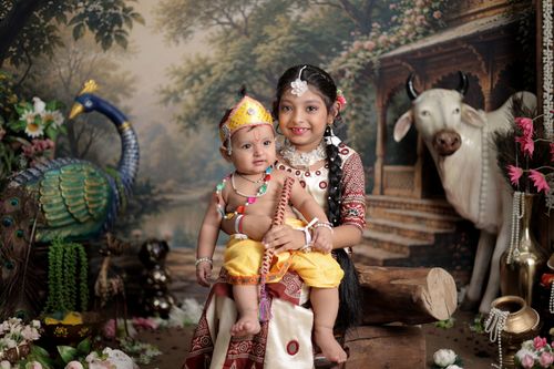 Free Two children in Indian costumes sitting with a decorative peacock and cow backdrop. Stock Photo