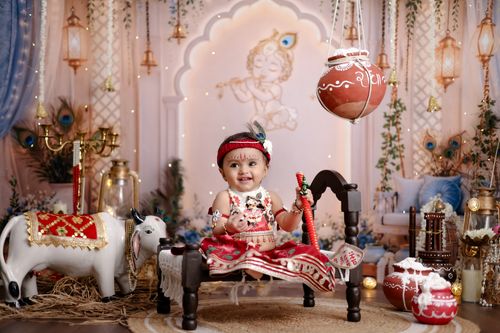 Free Smiling baby dressed as Lord Krishna in a festive setting with traditional decorations and a toy cow. Stock Photo