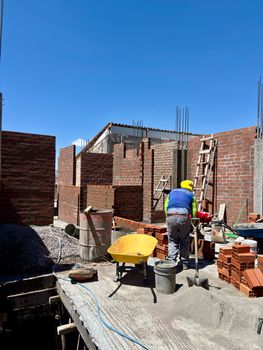 A worker at a brick construction site in Ayacucho, Peru, under a clear blue sky.