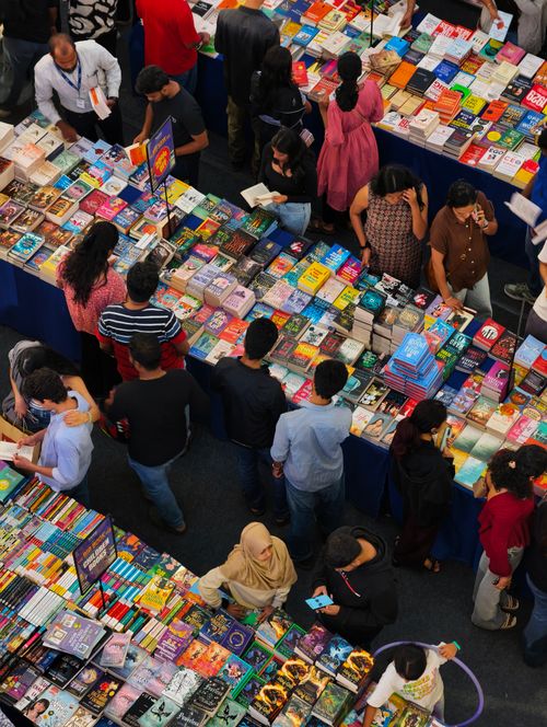 Free Colorful book fair overhead view with diverse crowd browsing literature. Stock Photo