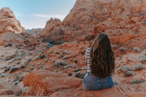 Free Woman in Blue Denim Shorts Sitting on Brown Rock Mountain Stock Photo