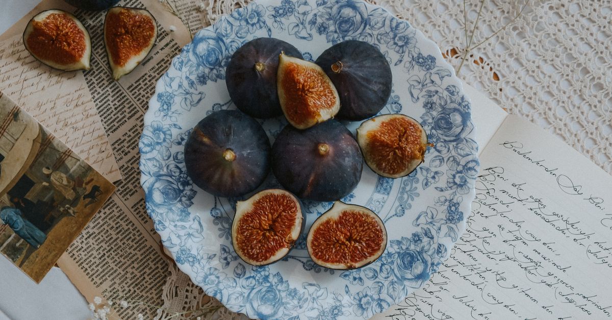 A beautifully arranged still life of figs on a floral plate surrounded by vintage papers, creating a rustic and elegant vibe.