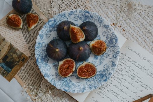 A beautifully arranged still life of figs on a floral plate surrounded by vintage papers, creating a rustic and elegant vibe.