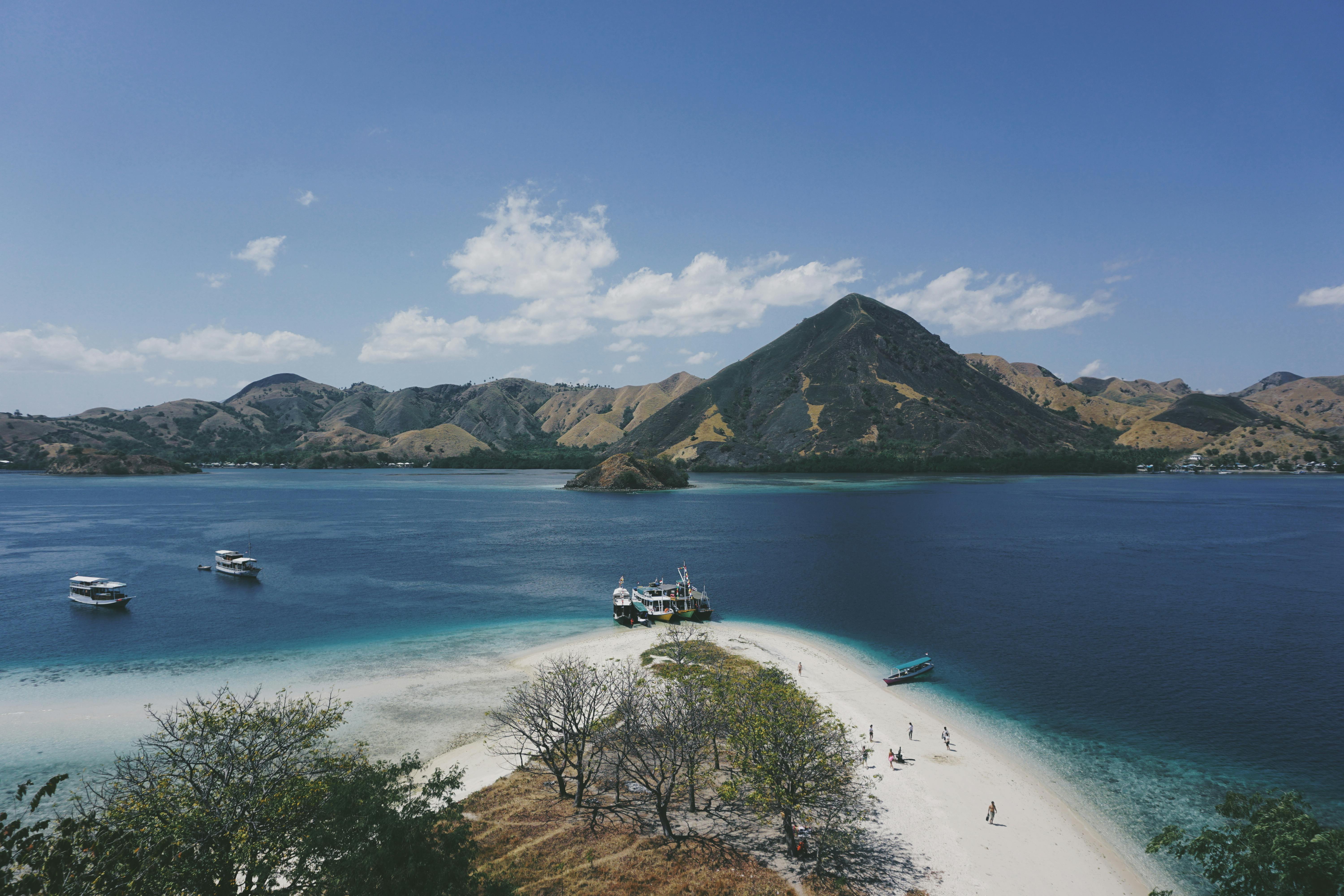 Rinca Island scenery during a Labuan Bajo cruising experience, featuring white sand beaches, anchored boats, turquoise waters, and rugged hills within Komodo National Park