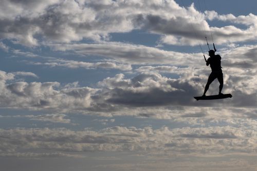 Free Silhouette of a kitesurfer airborne against a dramatic cloudy sky, capturing a sense of adventure. Stock Photo