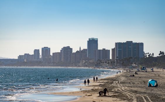 People enjoying a sunny day along Long Beach shore with city skyline in the background.