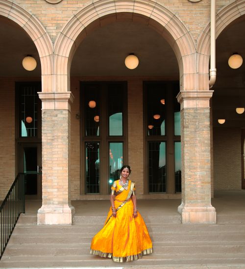 Free A woman wearing a vibrant sari poses gracefully in front of an elegant building with arched architecture. Stock Photo