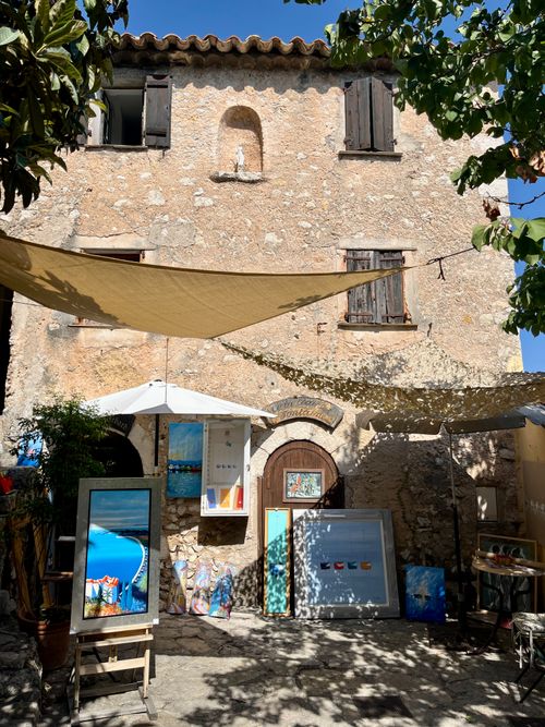 Free An artistic setup in Èze, France, features colorful paintings against a rustic stone house. Stock Photo