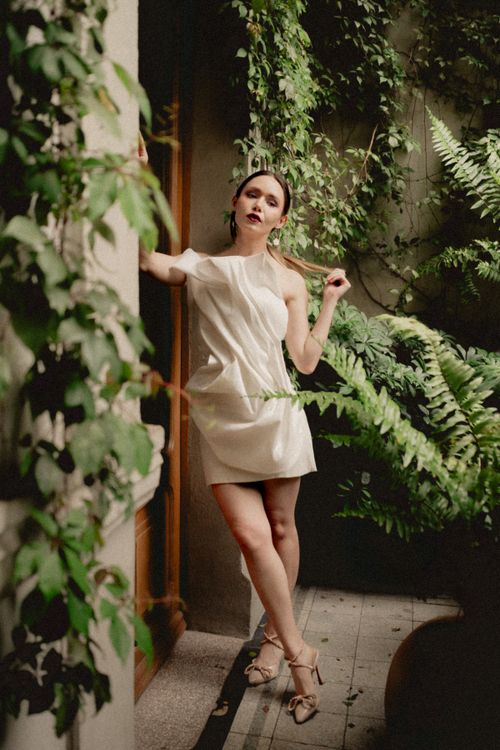 Free Elegant woman in a white dress posing in lush indoor garden. Fashion and nature blend in Mexico City. Stock Photo