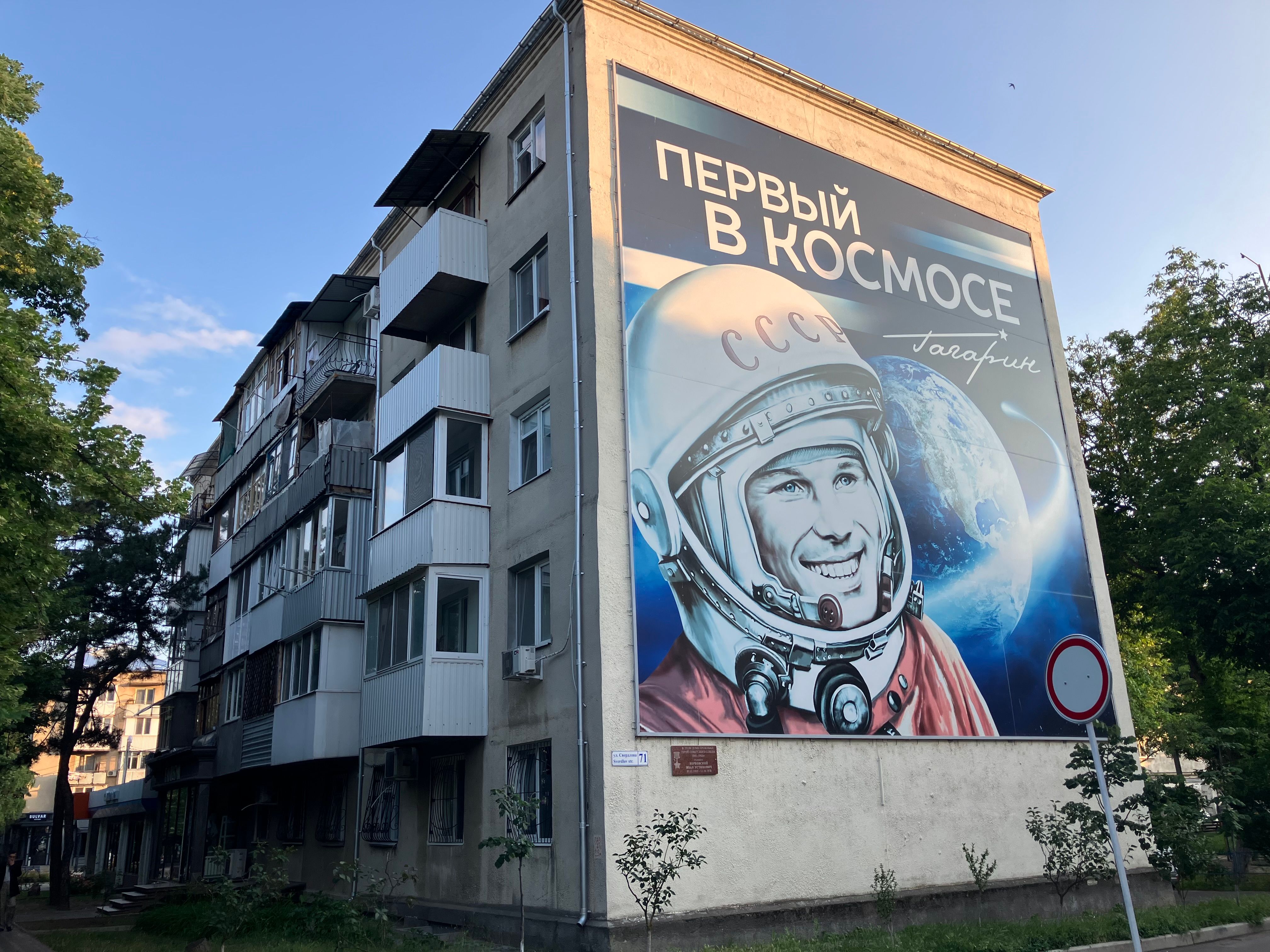 Large mural of a Soviet cosmonaut on a residential building under a clear sky.