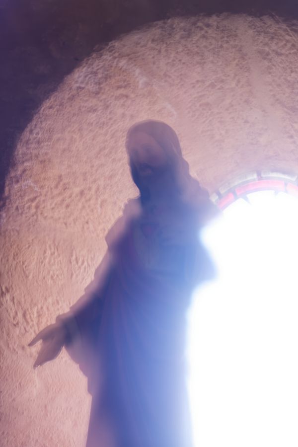 Statue floutée du Christ aux bras ouverts, baignée de lumière