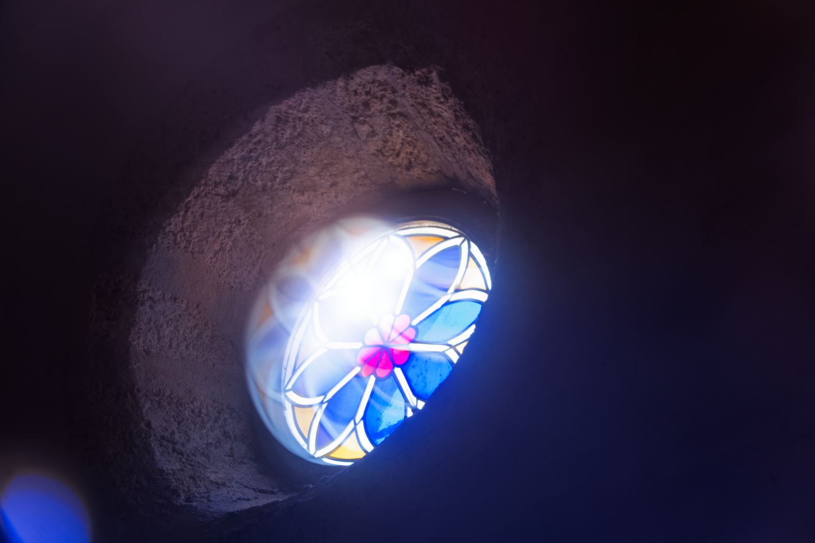 Vitrail bleu et rose illuminant un mur d'église en pierre