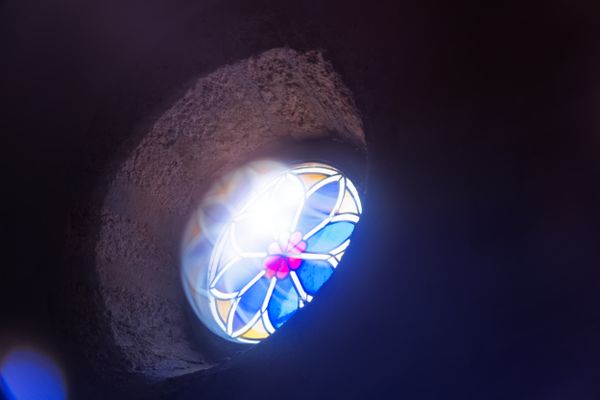 Vitrail bleu et rose illuminant un mur d'église en pierre