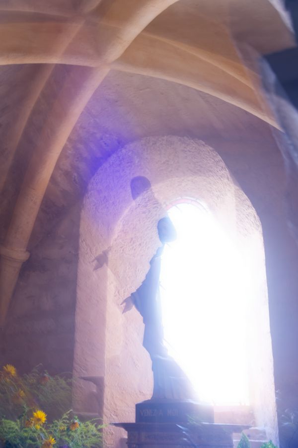 Statue du Christ dans une alcôve de pierre au-dessus de fleurs jaunes, chemin de Compostelle