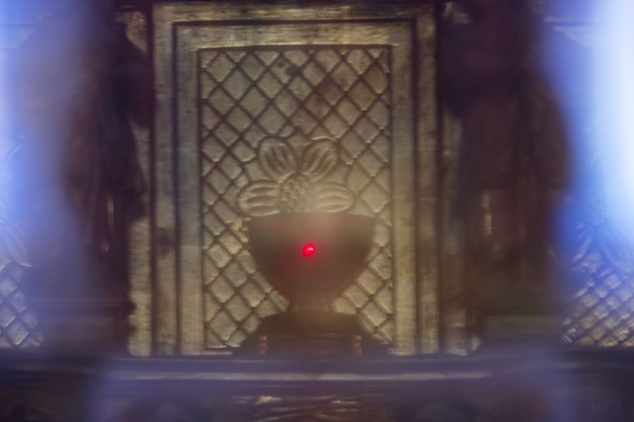 Votive lamp and carved altar panel viewed through a dim archway